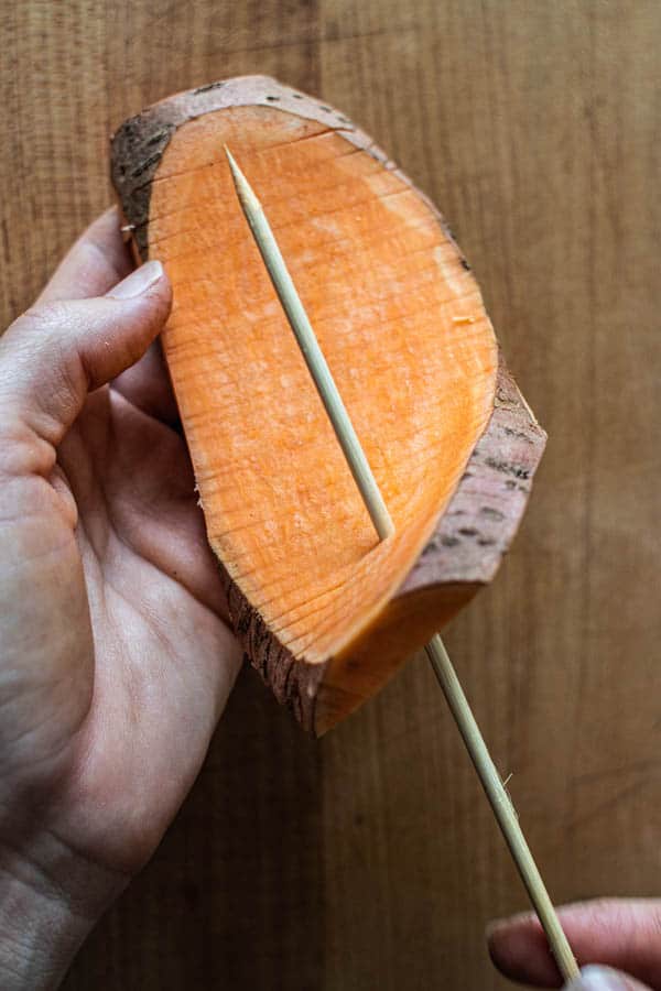 A slab of sweet potato that has been sliced vertically and horizontally to create an accordion pattern is being threaded onto a wooden skewer.