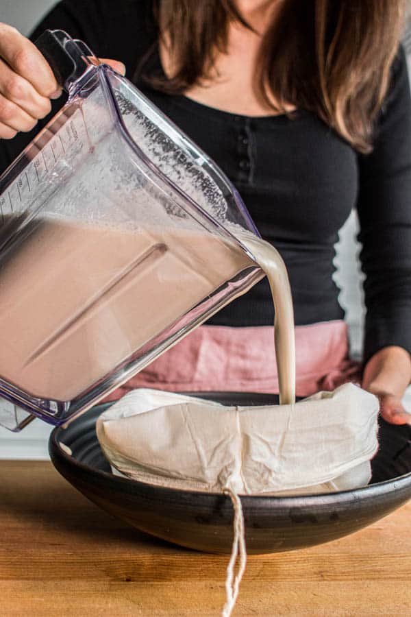 This is how to make almond milk! Blended almond, prune, and water mixture being poured into a nut milk bag that is set inside a large bowl for straining. 