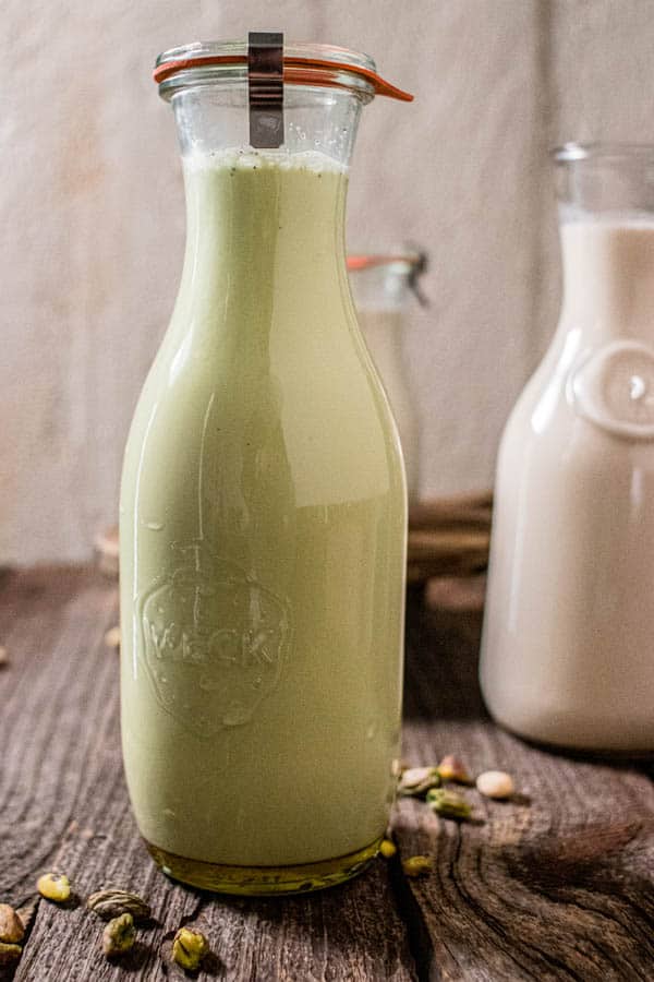 A carafe of pistachio milk on a table next to a carafe of pistachio milk.