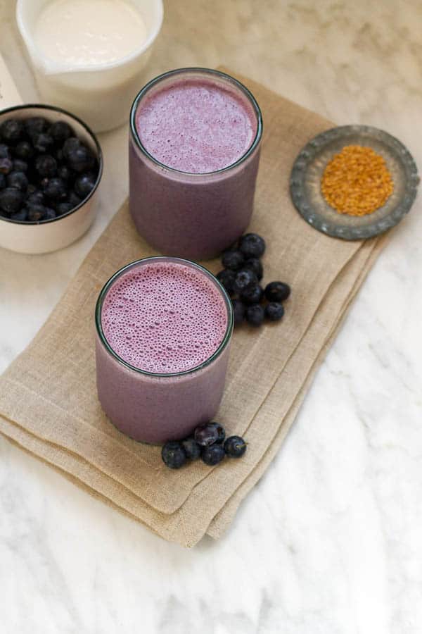 Two Blueberry Banana Almond Butter Smoothies on a table with fresh blueberries.