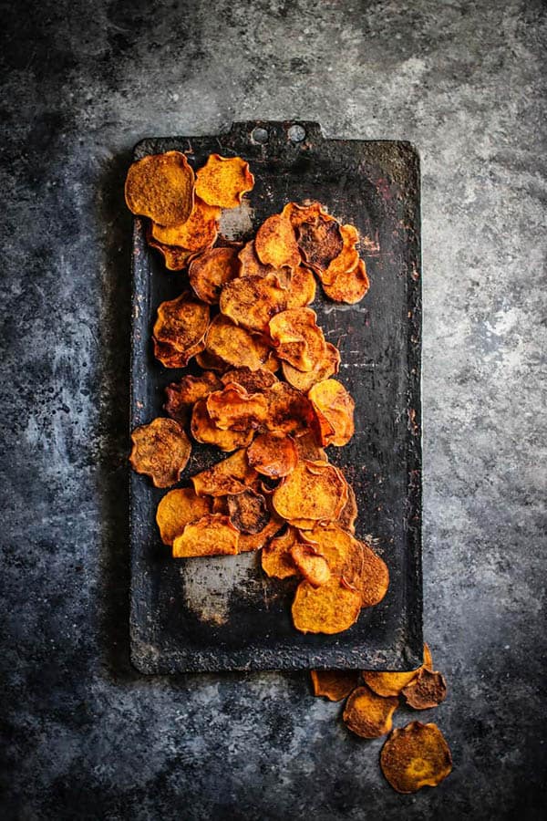 A scattering of golden, Honey BBQ Sweetpotato Chips on a black serving tray .