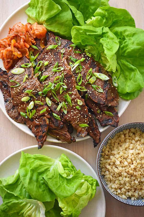 A close up of a platter of Kalbi recipe served with lettuce cups, cauliflower rice and kimchi.