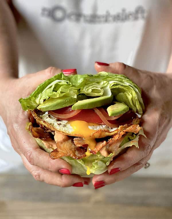 A woman holding a Cobb salad inspired sandwich that has lettuce cups instead of bread. 