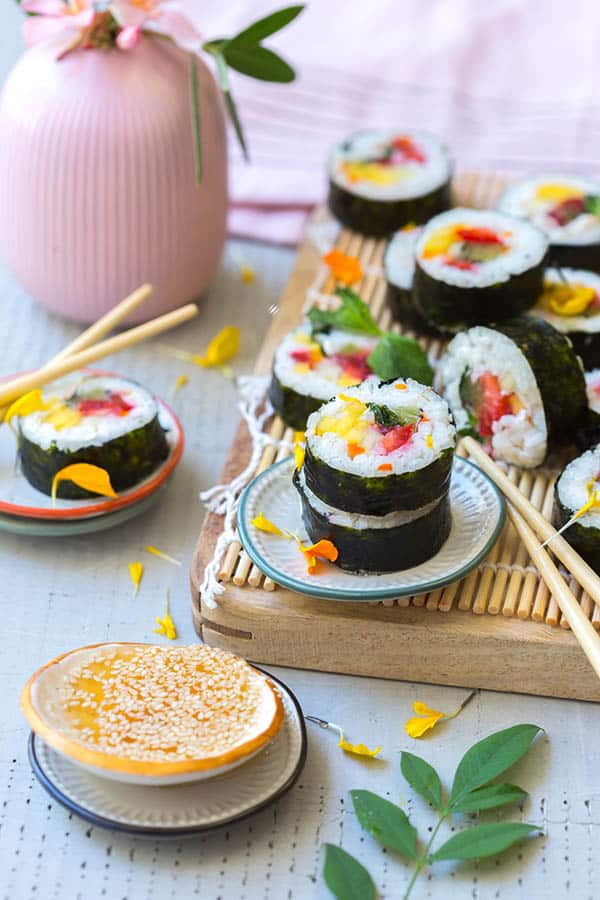 Fruity Coconut Kimbap filed with kiwi, berries, mangoes and sticky rice then wrapped in a sheet of seaweed and sliced like slices of sushi are stacked on a serving plate with chopsticks.