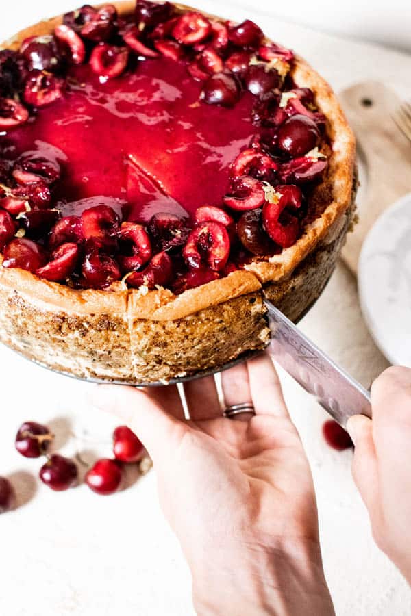 A slice of Fresh Cherry Cheesecake  being cut from the whole cake. 