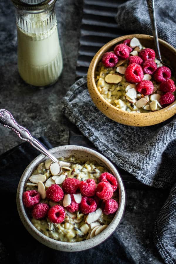 Two bowls of pistachio wild rice pudding on a table next to a bottle of pistachio milk. This easy recipe for rice pudding is best served with fresh berries and almonds.