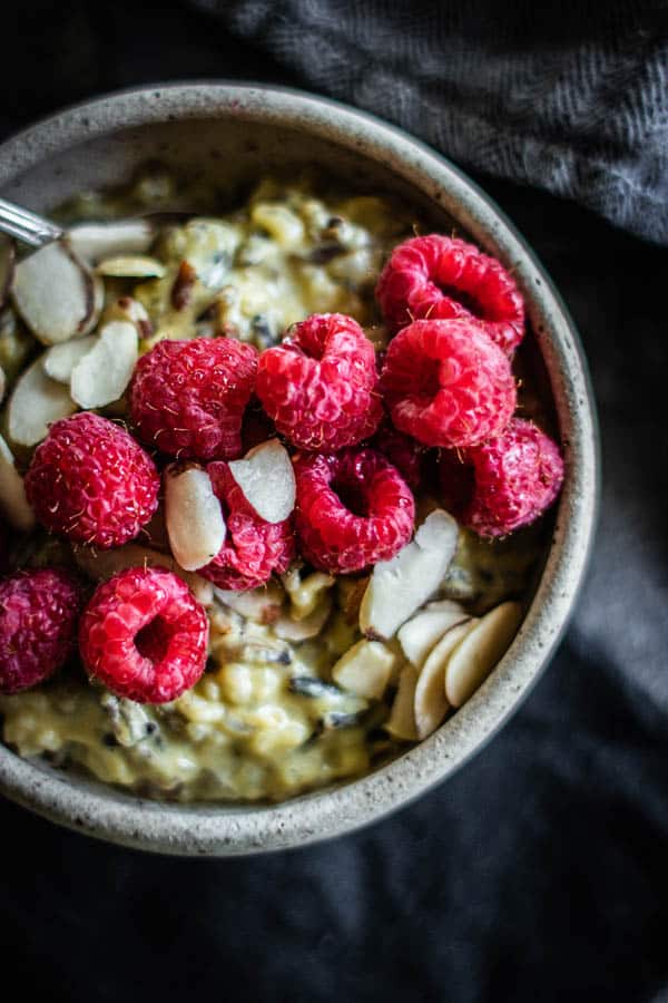 Close up of a bowl of Pistachio Wild Rice Pudding topped with fresh raspberries and toasted almonds. This easy recipe for rice pudding is simple to make and good for you too.