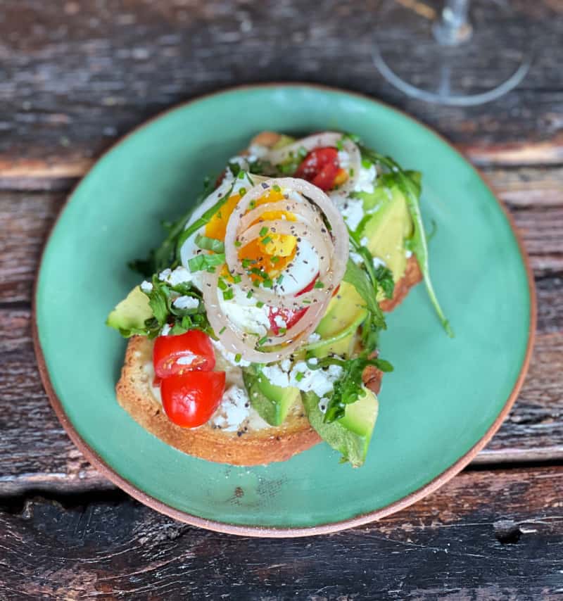 finished avocado toast with fried egg, arugula, tomatoes, olive oil