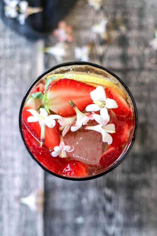 A cocktail with lemon wheels, strawberries, and edible flowers.