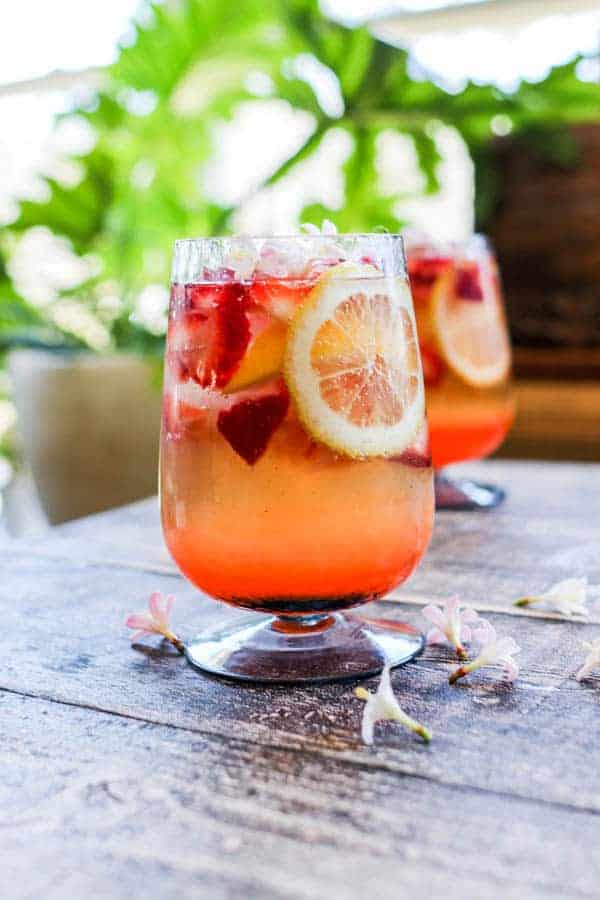 A cocktail with lemon wheels, diced strawberries and edible flowers.