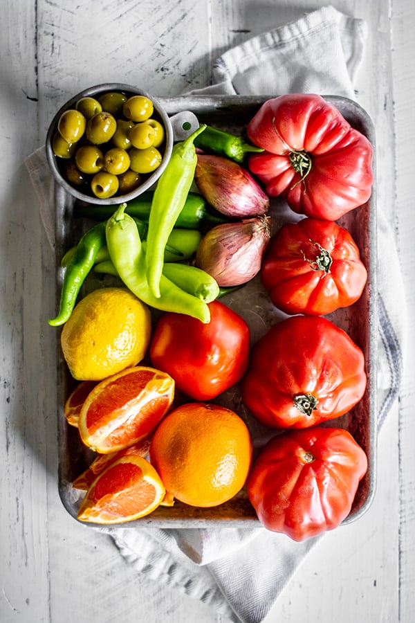 All of the fresh ingredients needed to make our homemade Bloody Mary mix recipe. Tomatoes, peppers, oranges, olives, lemons and shallots.