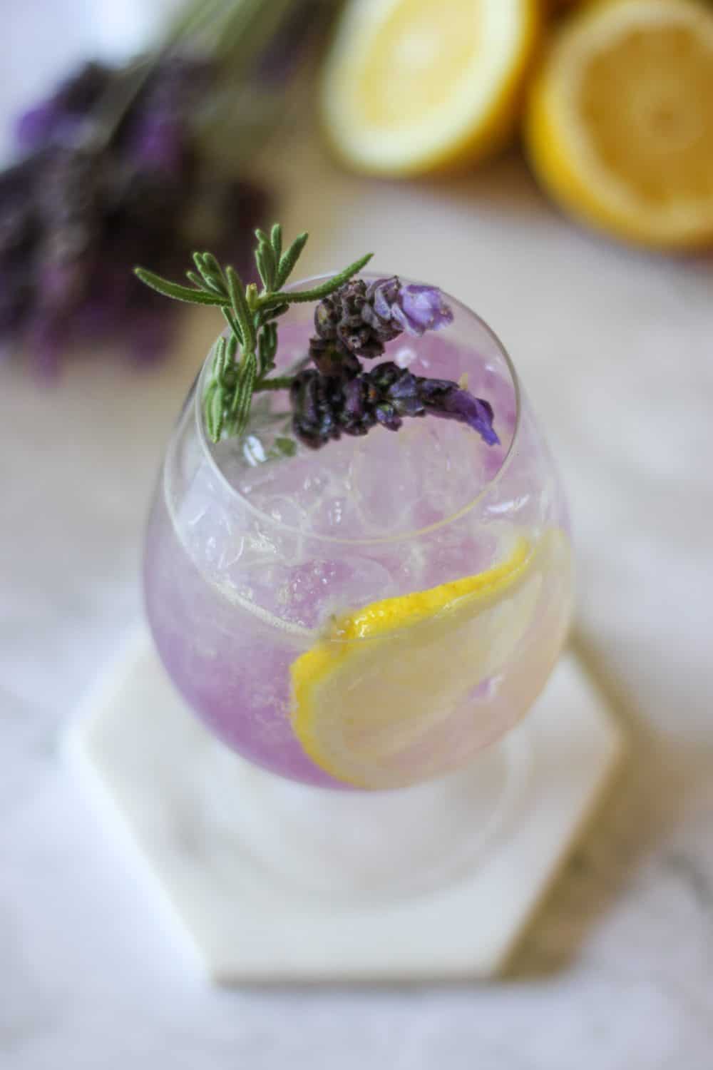 A Lemon Lavender Summer Gin Spritz on a white coaster next to lemon wheels.