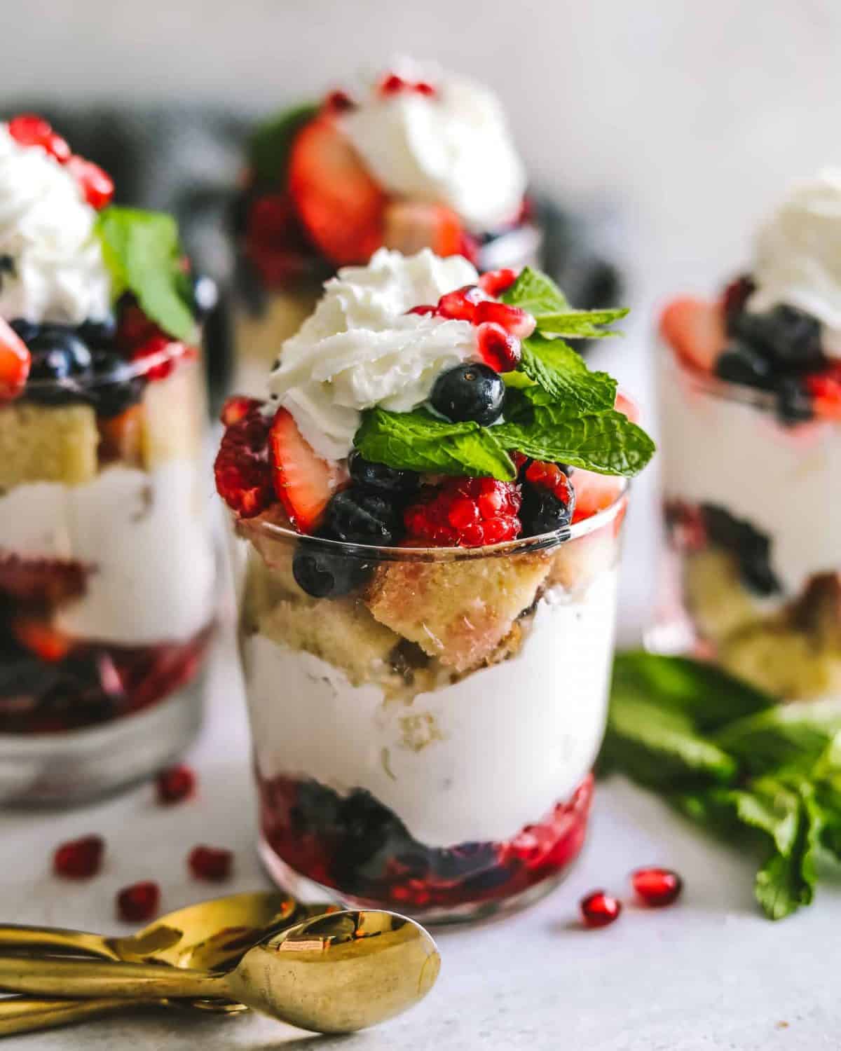 A red, white and blue dessert trifle in a small glass with layers of pomegranate arils and blueberries, whipped cream, and butter cake. 