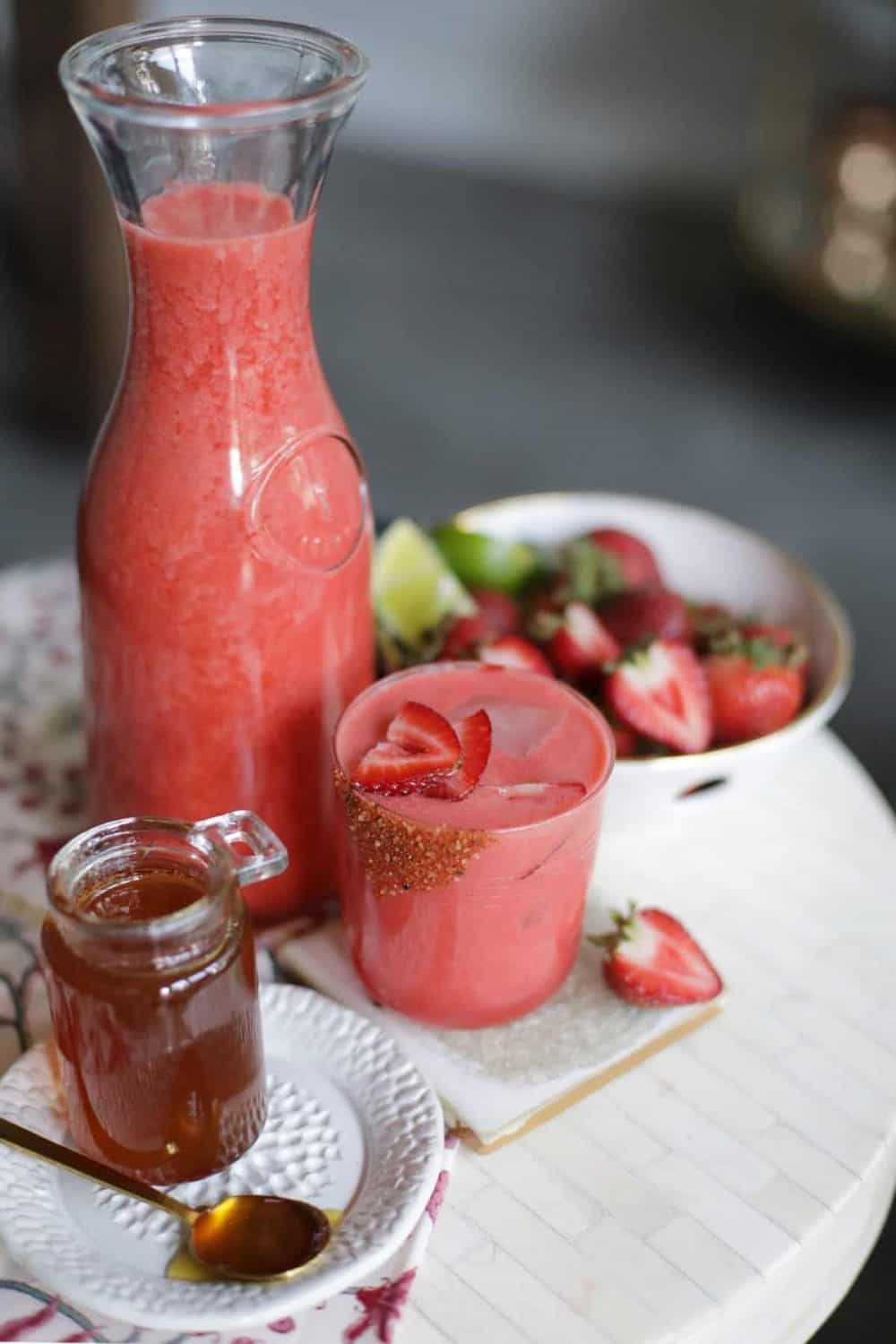 Easy Strawberry Agua Fresca in a jug next to a small jar of honey and a bowl of berries.