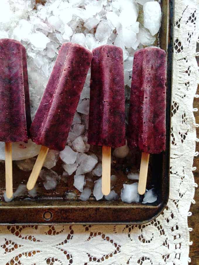 Homemade popsicles, lemon blueberry verbena flavored on a tray with ice underneath it.