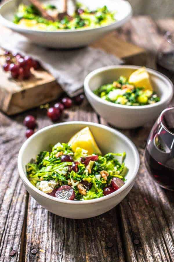 Bowls of kale and grape salad with lemon wedges.