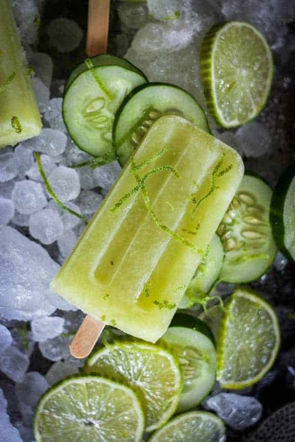 A cucumber Limeaid homemade popsicle on a bed of ice, cucumber wheels and lime wheels.