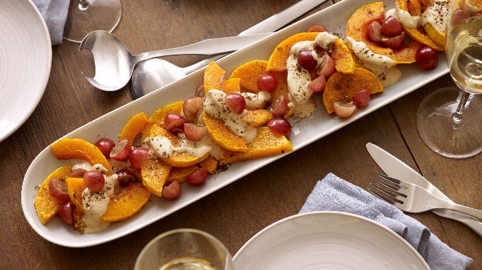 A beautiful long oval platter filled with slices of roasted winter squash, red grapes, and tahini.