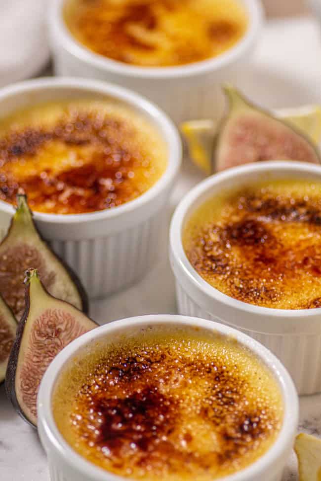 Ramekins of Fresh Fig Compote and Easy Crème Brûlée on a table with fresh halved figs and lemon slices.