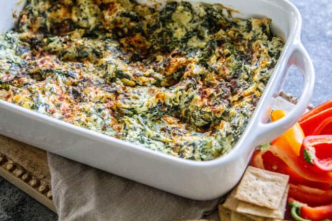 A Classic Artichoke and Spinach Dip Recipe served with crackers and halved bell peppers.