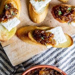 Crostini piled high with slices of breakfast cheese and sweet onion jam. A bowl of sweet onion jam sits off to the side.