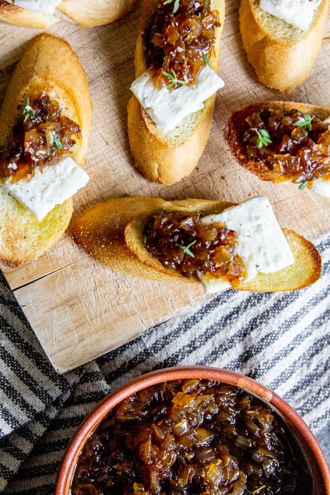 Crostini piled high with slices of breakfast cheese and sweet onion jam. A bowl of sweet onion jam sits off to the side.