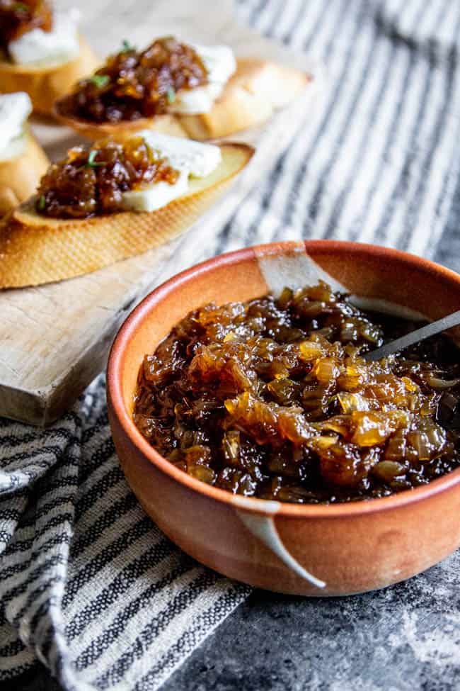 A bowl of sweet onion jam next to crostini.