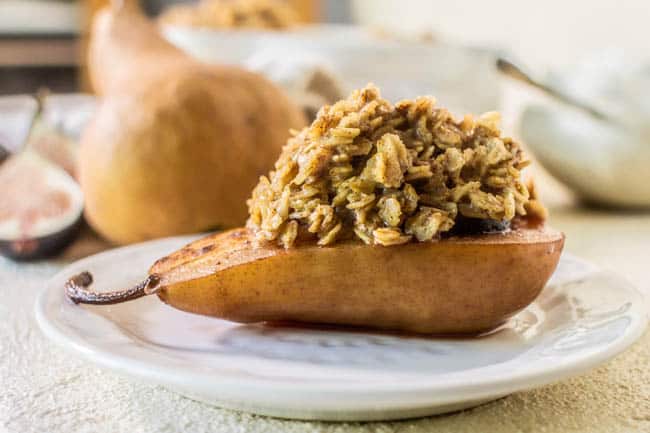 A roasted pear half on a serving  plate piled high with oatmeal. This Recipe for Baked Oatmeal Fig Stuffed Pears has a fig nestled inside the pear.