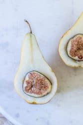 A pear that has been sliced in half and had the seeds and core removed. Half of a fresh fig is nestled inside each pear half. This is the first step in thsi recipe for baked oatmeal and fig stuffed pears..