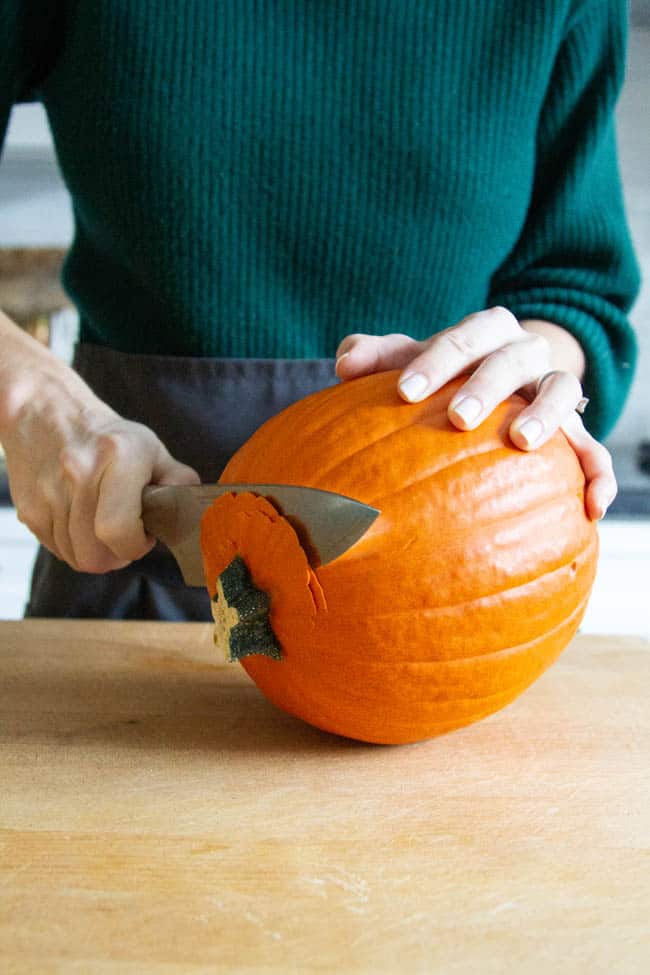 A woman removing the stem from a pumpkin.