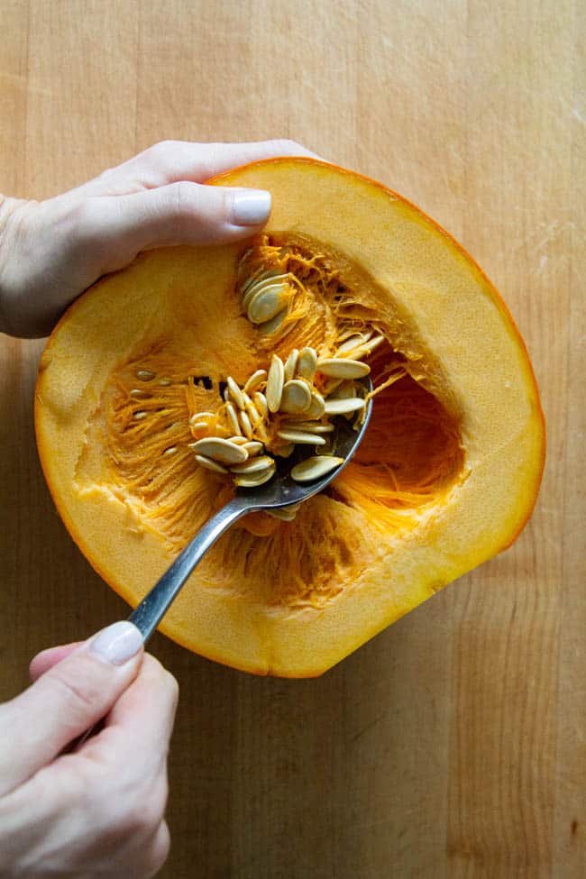 A halved pumpkin with the seeds being scooped out.
