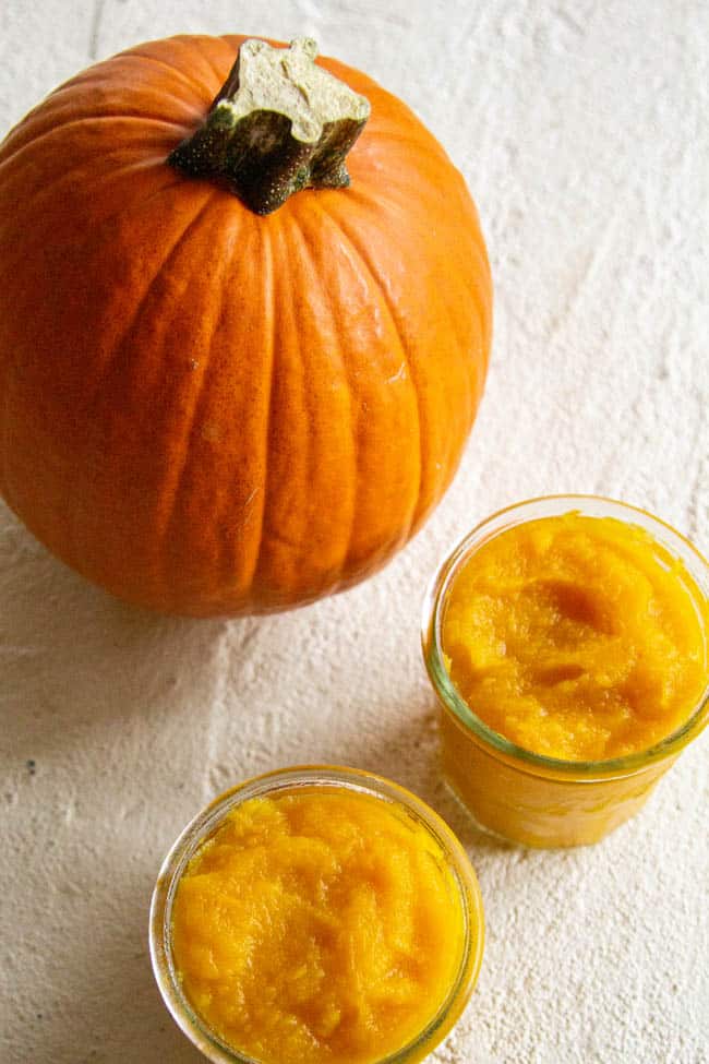 pumpkin puree in two containers next to a pumpkin.
