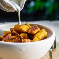 A bowl of Pumpkin and Roasted Sweet Potato Gnocchi. Cream is being drizzled over the gnocchi.