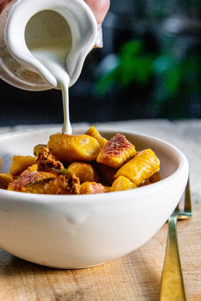 A bowl of Pumpkin and Roasted Sweet Potato Gnocchi. Cream is being drizzled over the gnocchi.