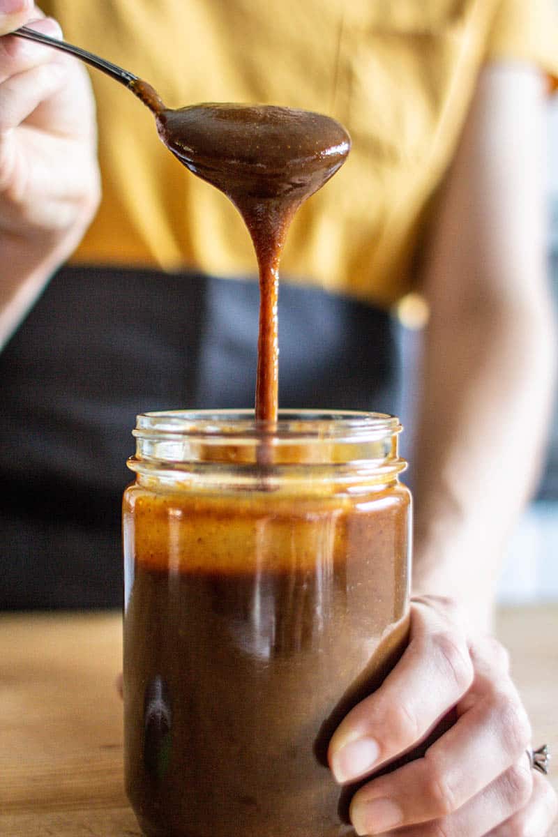 A woman drizzling prune pureé from a spoon into a jar.