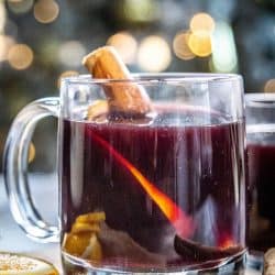 A mug of mulled wine in front of a Christmas tree with twinkle lights.