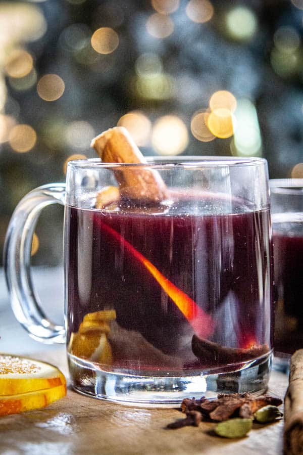 A mug of mulled wine in front of a Christmas tree with twinkle lights.