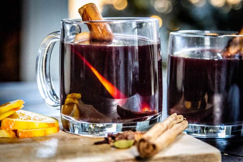 Two glasses of mulled wine with cinnamon sticks and orange slices.