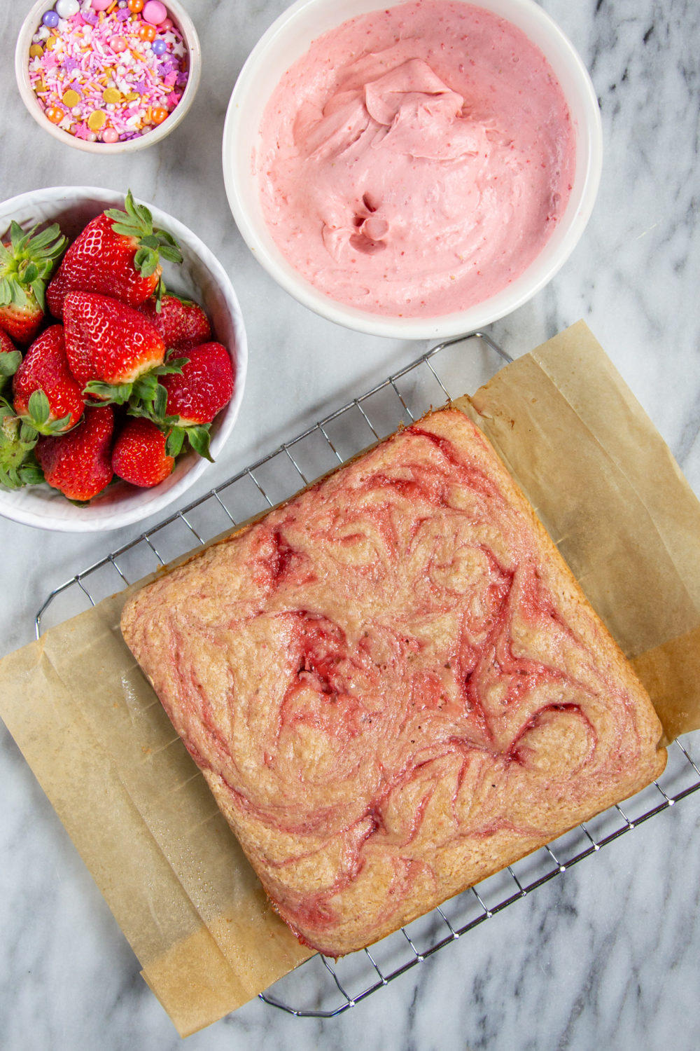 Strawberry Rosé Snack Cake not frosted with a bowl of strawberry rose cream cheese icing on the side and fresh berries.