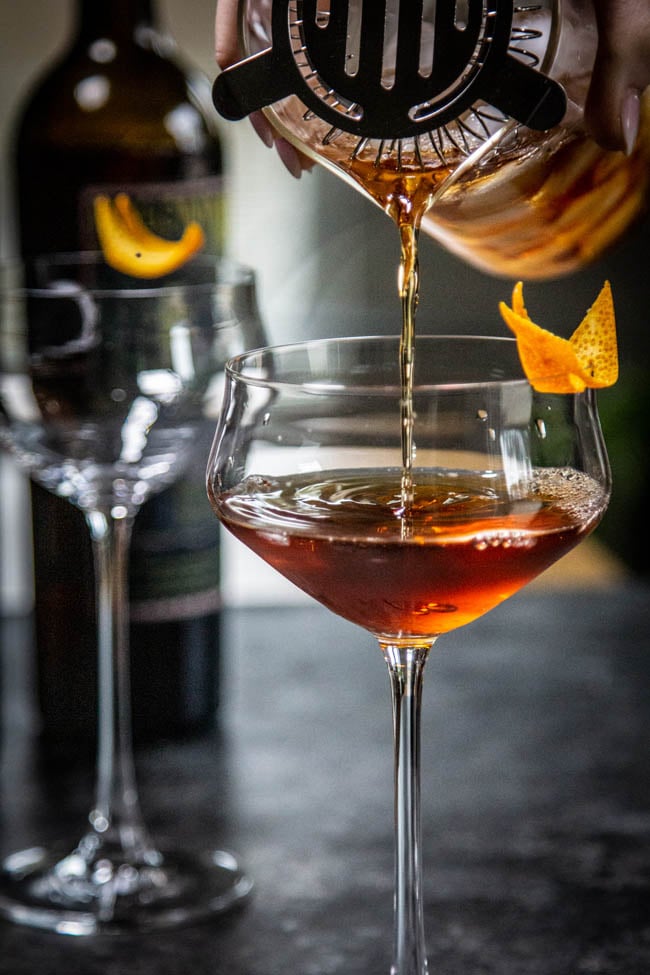 Adonis cocktail with vermouth being strained into a coupe glass.