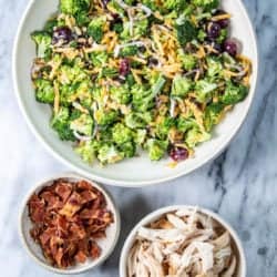 Broccoli Salad in a big serving bowl next to shredded rotisserie chicken and chopped bacon.
