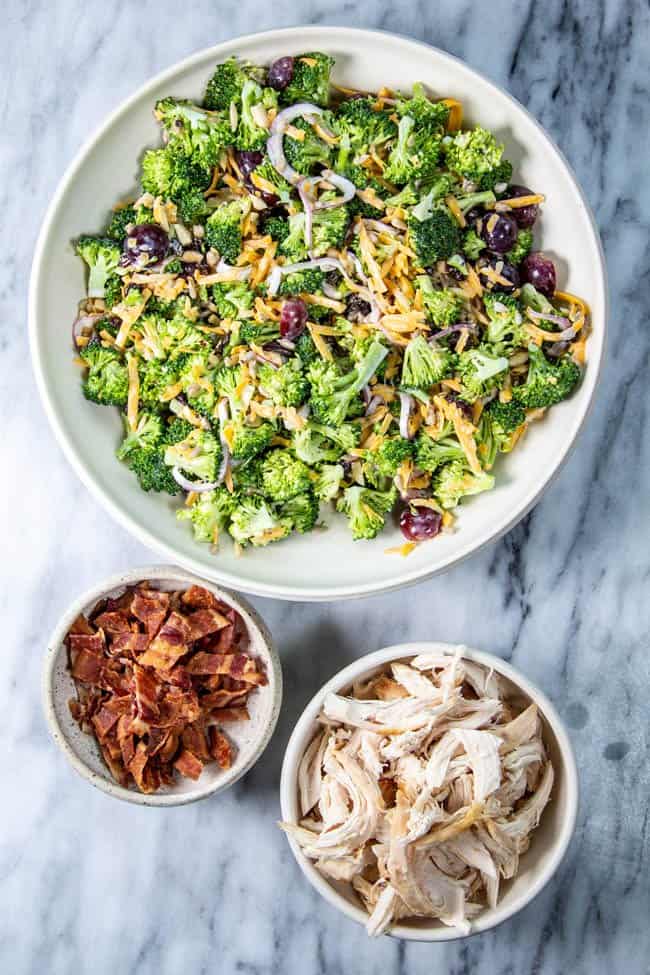 Broccoli Salad in a big serving bowl next to shredded rotisserie chicken and chopped bacon.