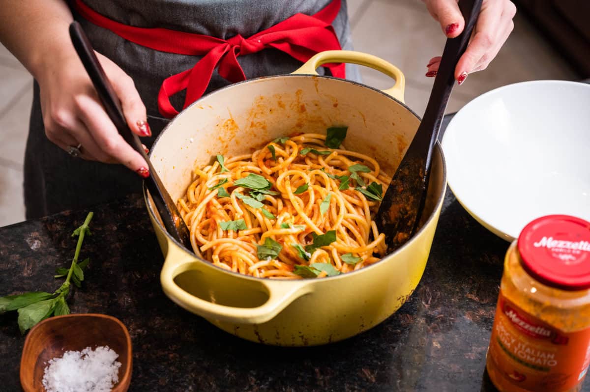 Woman stirring Mezzetta Sauce in to a bowl of pasta