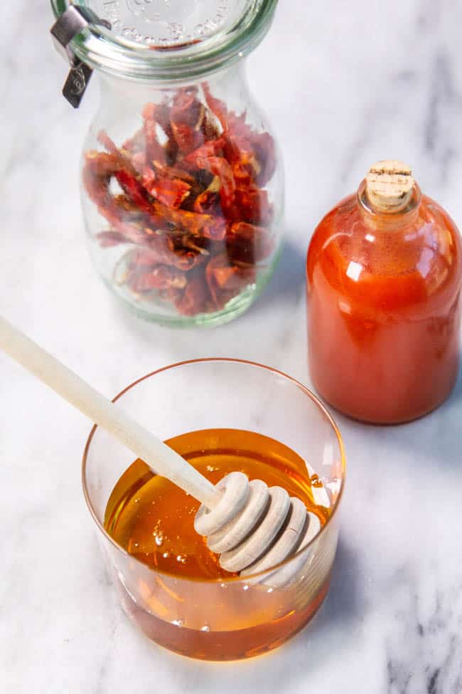 A jar of peppers and a jar of hot sauce next to a small bowl of honey. 