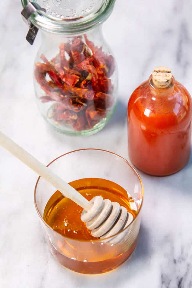 A jar of peppers and a jar of hot sauce next to a small bowl of honey.