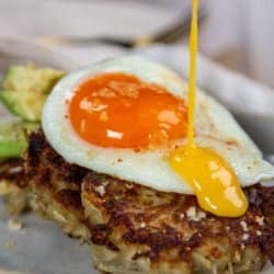 California Avocado & Eggs Benedict with Crispy Potato Cakes being drizzled in hollandaise sauce.