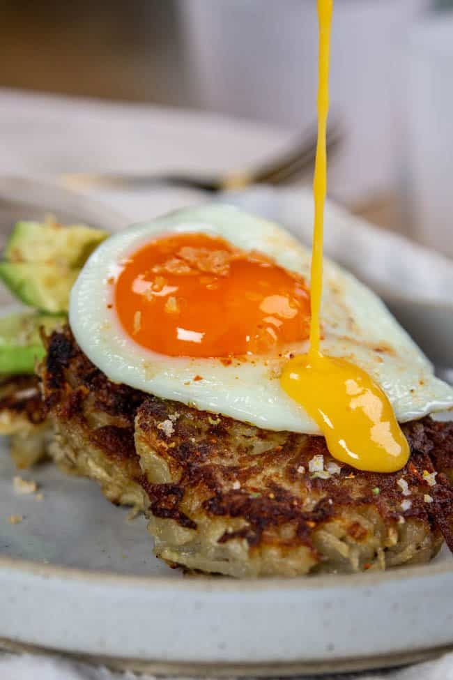 California Avocado & Eggs Benedict with Crispy Potato Cakes being drizzled in hollandaise sauce.