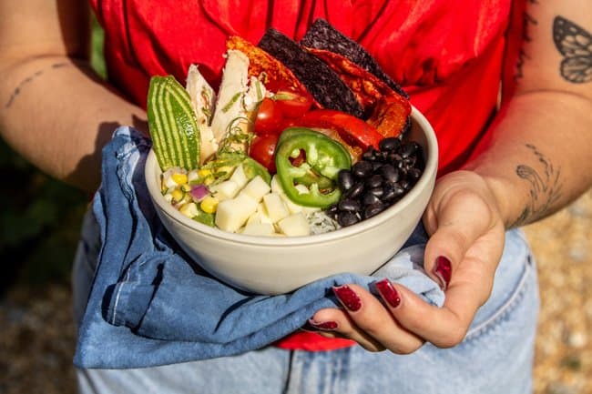 A girl with red nails and shirt and blue jeans holding a red, white, and blue burrito bowl