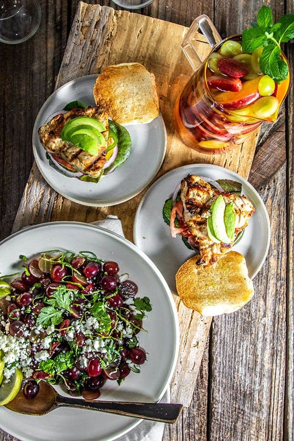 The Best Grape Recipes To Try Now! A meal set up with grilled chicken sandwiches on plates and sangria in cups.