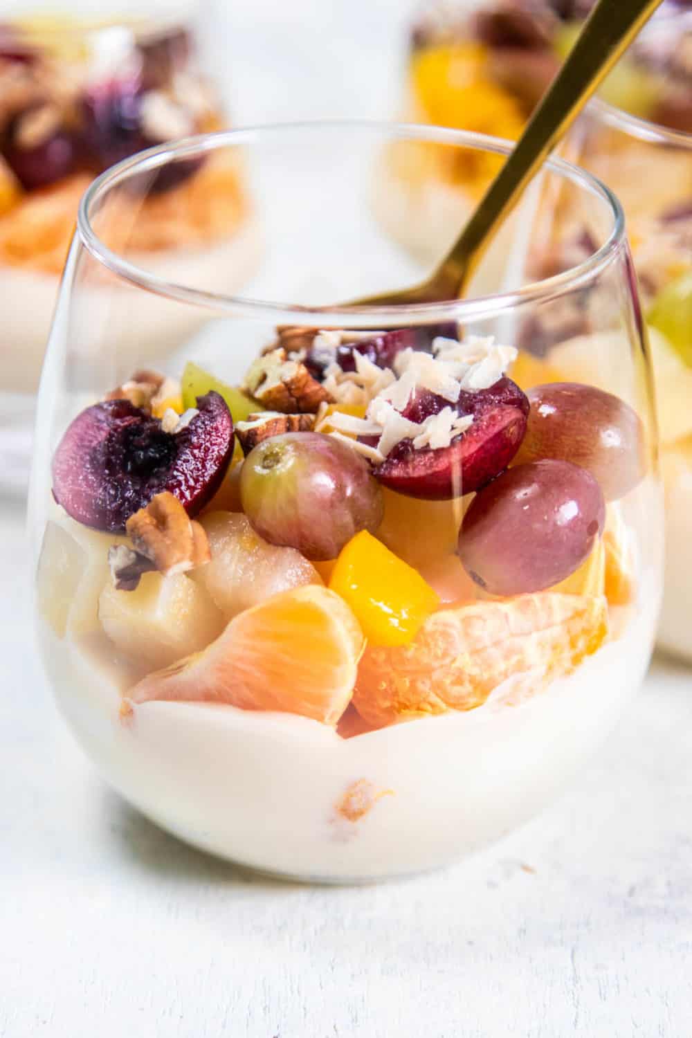 A close up of layered Ambrosia Salad with mandarins, grapes, cherries, pears, and peaches.